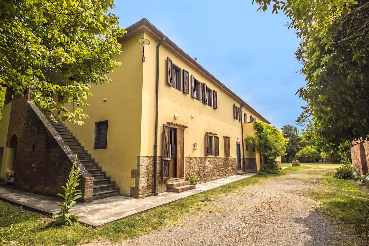 Bazén s modrými slunečníky a lehátky, v pozadí toskánský statek obklopený zelení